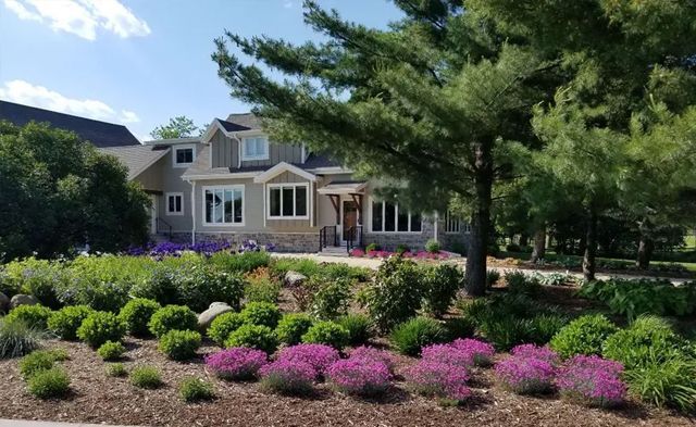 House with gray siding and lush landscaping, featuring purple flowers and trees.
