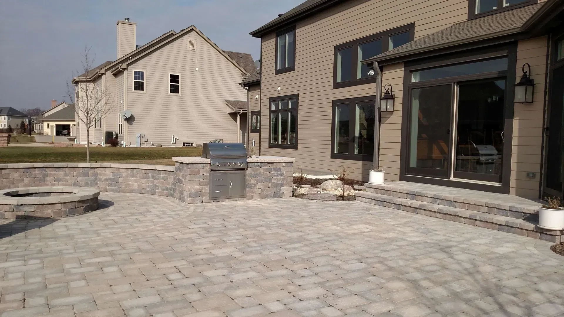 Backyard patio with brick pavers, fire pit, built-in grill, and a two-story brick house.