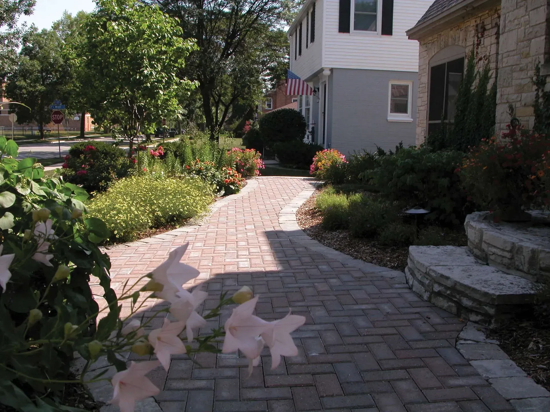 Brick walkway leading toward a two-story house with landscaped flower beds on either side.