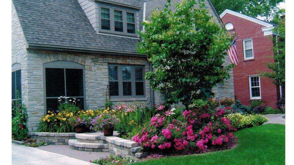 Stone house with flower garden; a red brick building is to the right.