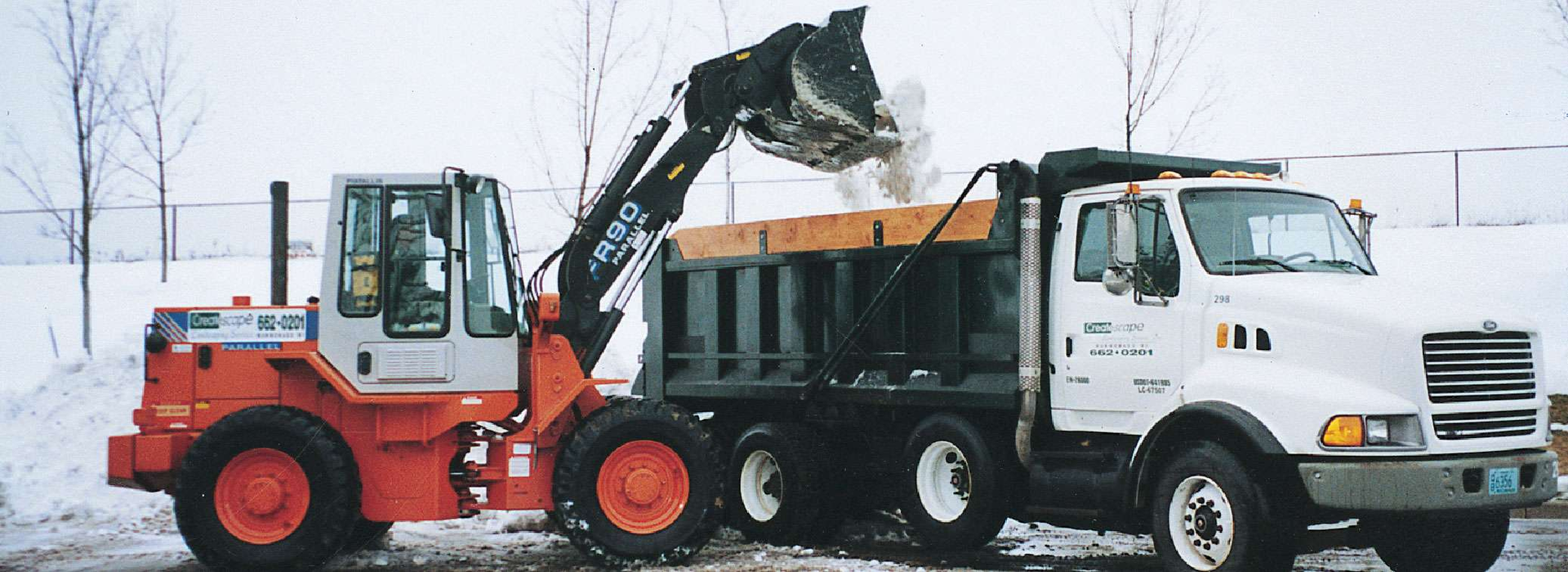 Orange and white loader filling a dump truck with snow. Winter scene.
