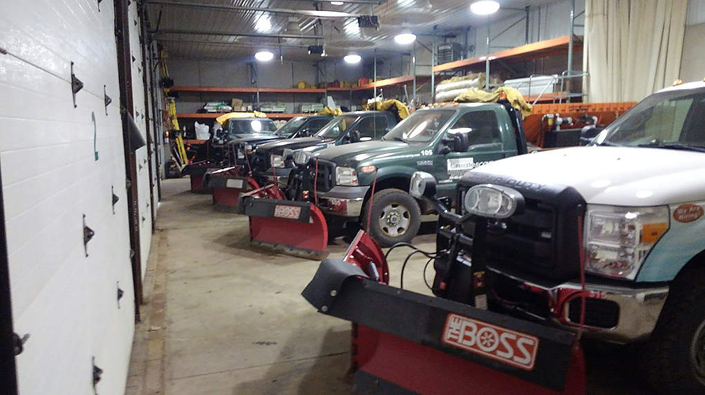 Snowplow trucks parked inside a garage, each with a red plow attached.