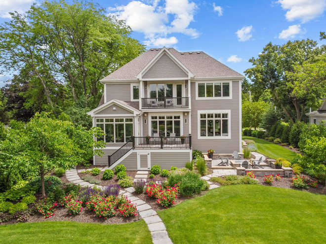 Two-story gray house with patio, balcony, and lush landscaping on a sunny day.