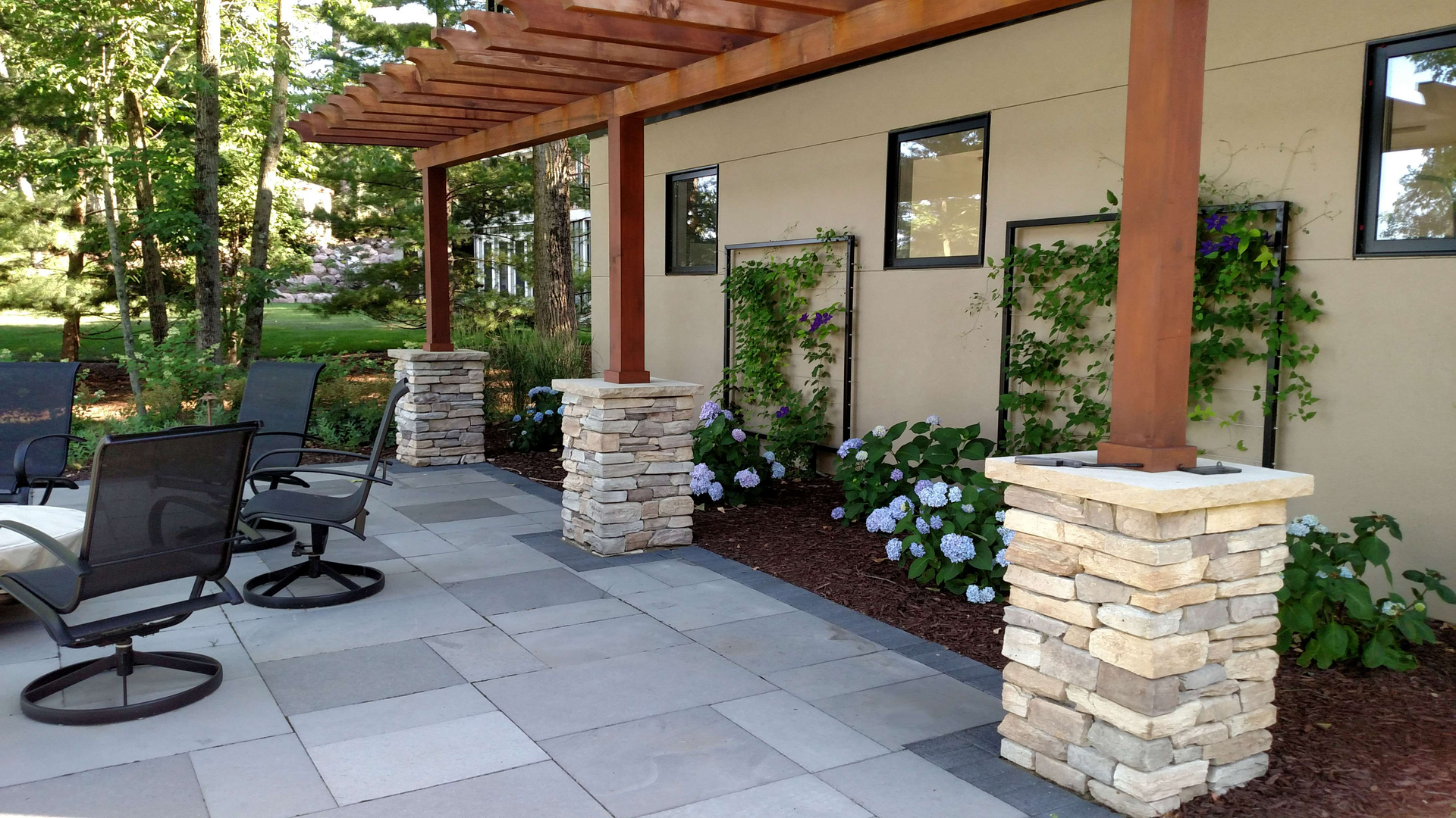 Patio with stone columns, pergola, gray pavers, seating, and climbing plants.