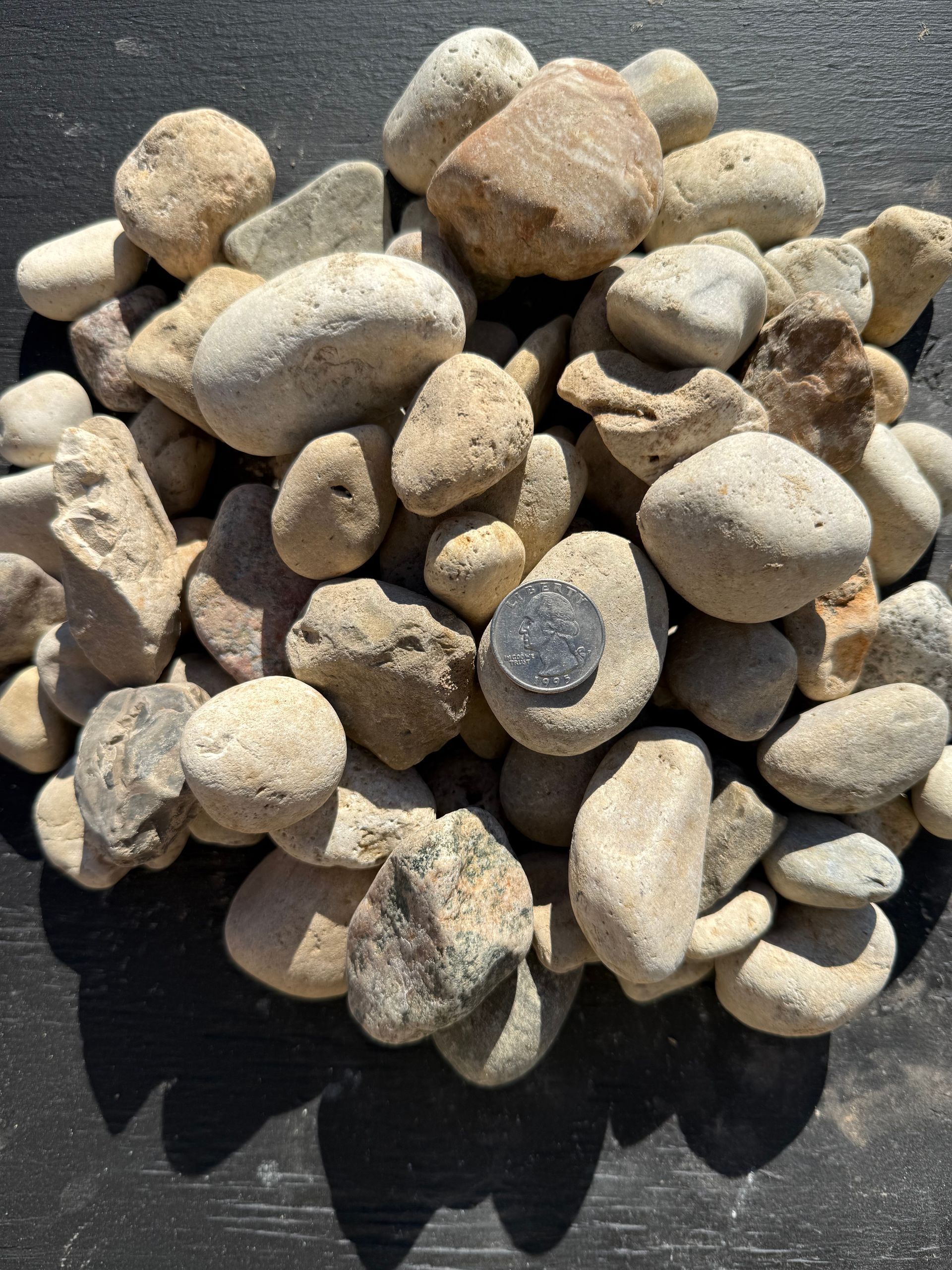 Pile of small beige and gray stones on a dark surface