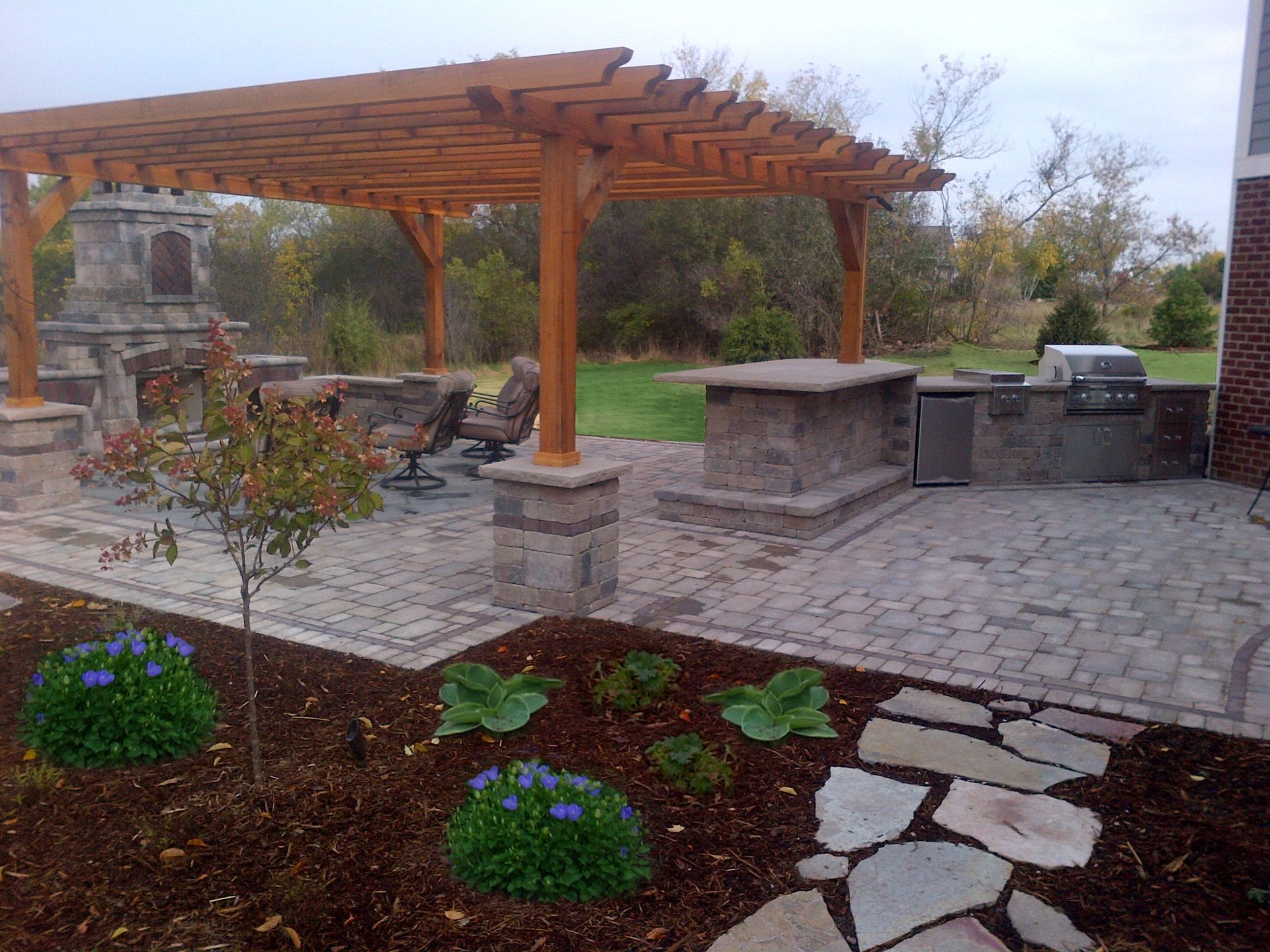 Outdoor patio with a wooden pergola, fireplace, and built-in grill.