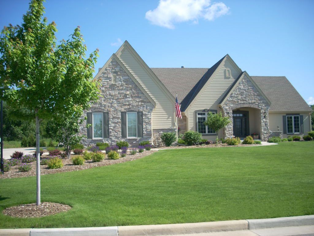 Single-story house with stone facade, green lawn, and landscaped flower beds.