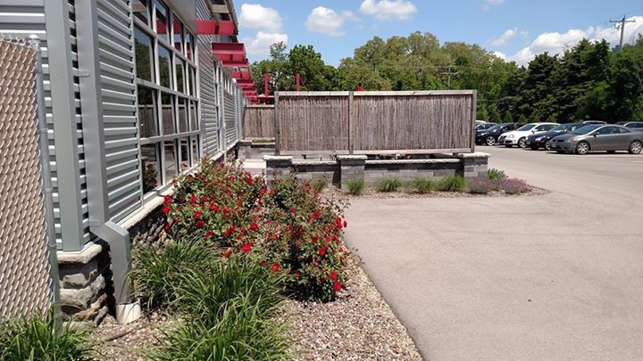 Building exterior with red trim and roses; wooden fence and parked cars on a sunny day.