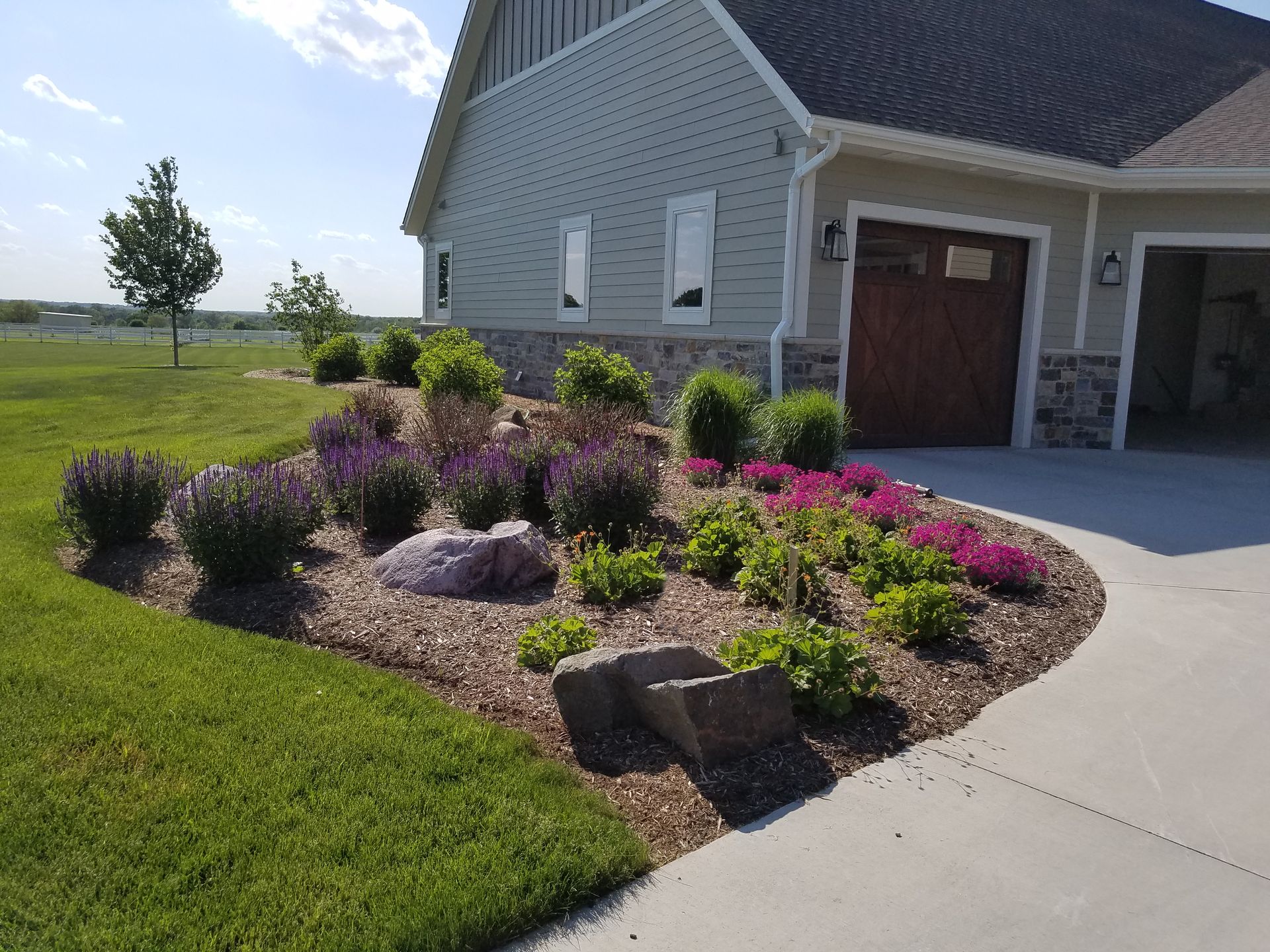 Landscaped flower bed with purple and pink blooms in front of a house.