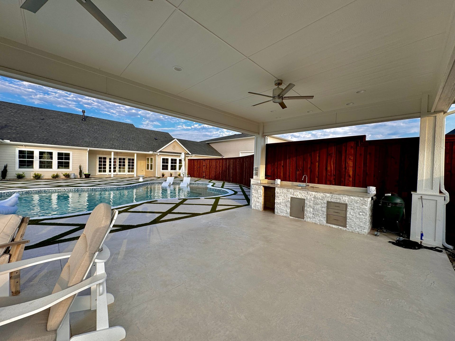 A patio with chairs and a ceiling fan overlooking a swimming pool.