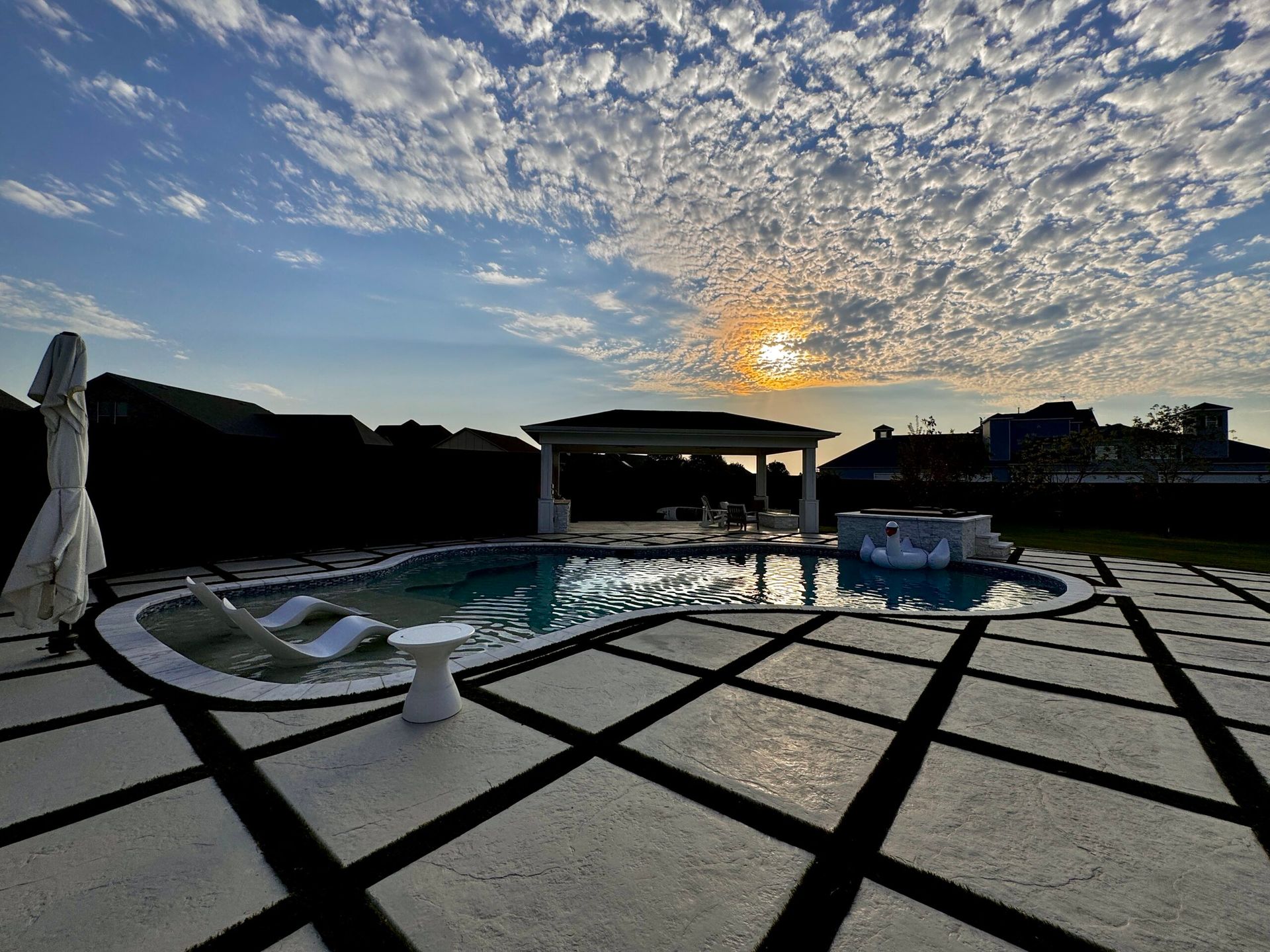 A large swimming pool with a gazebo in the background and a sunset in the background.
