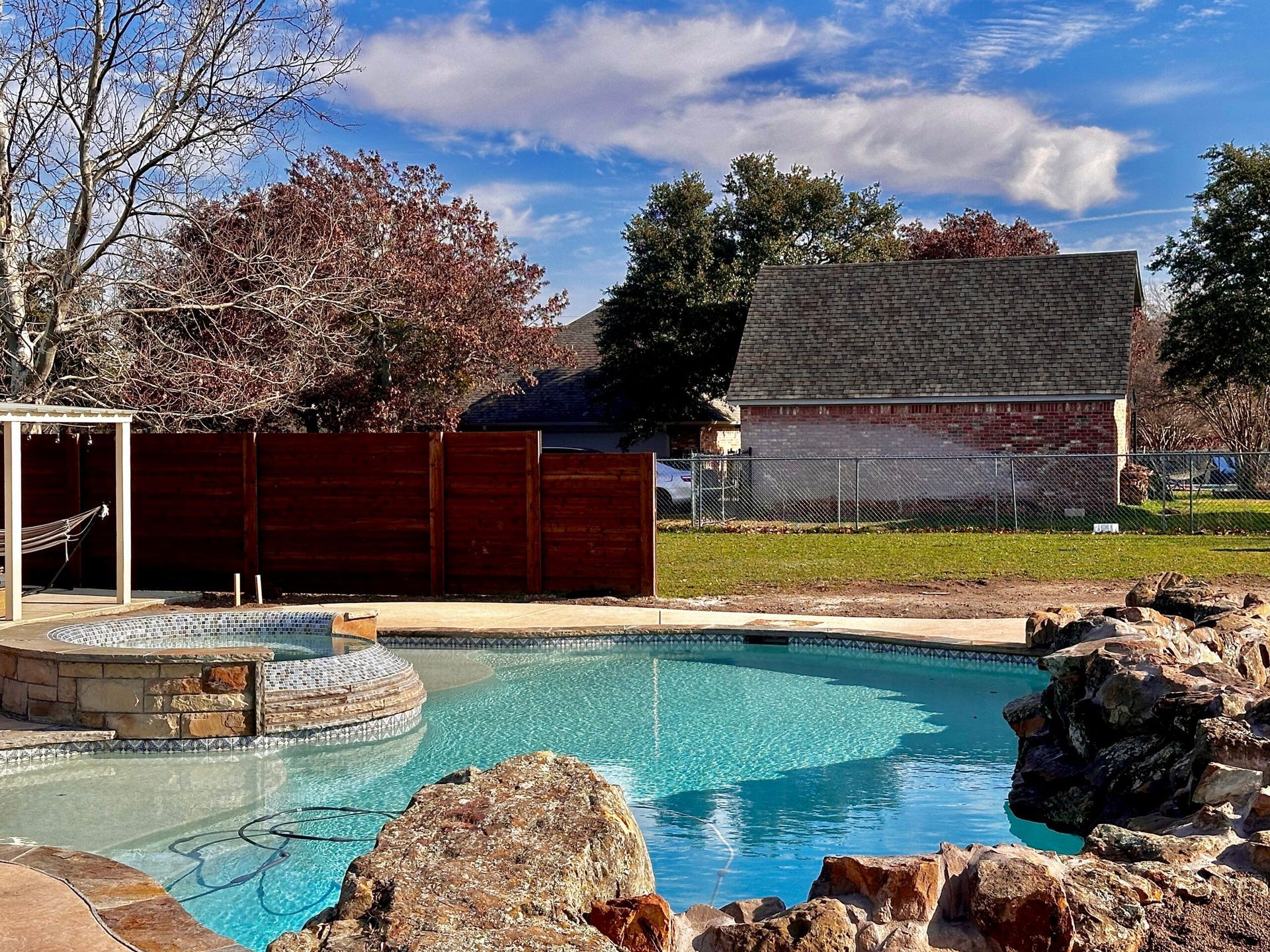 A large swimming pool is surrounded by rocks and a fence.