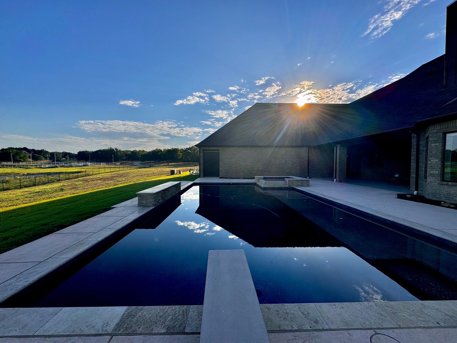 A large swimming pool in front of a house with the sun shining through the clouds