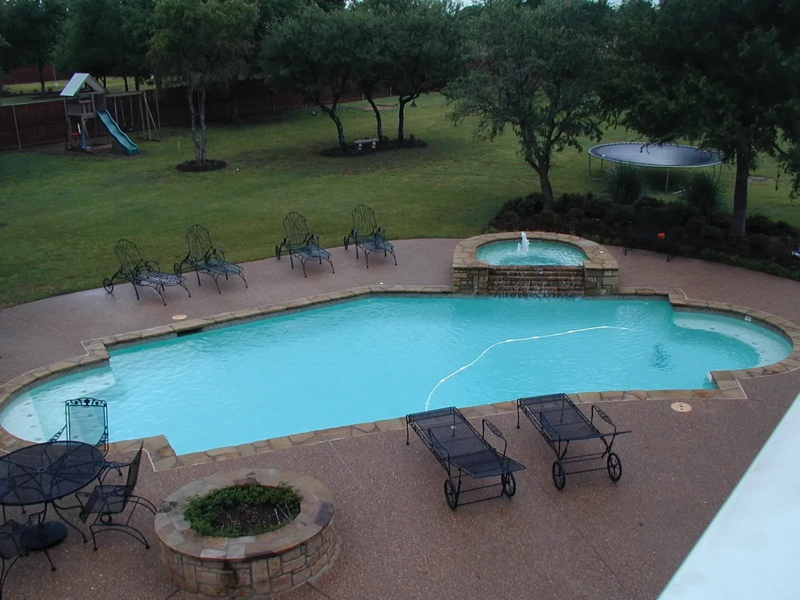 A large swimming pool surrounded by chairs and a fire pit