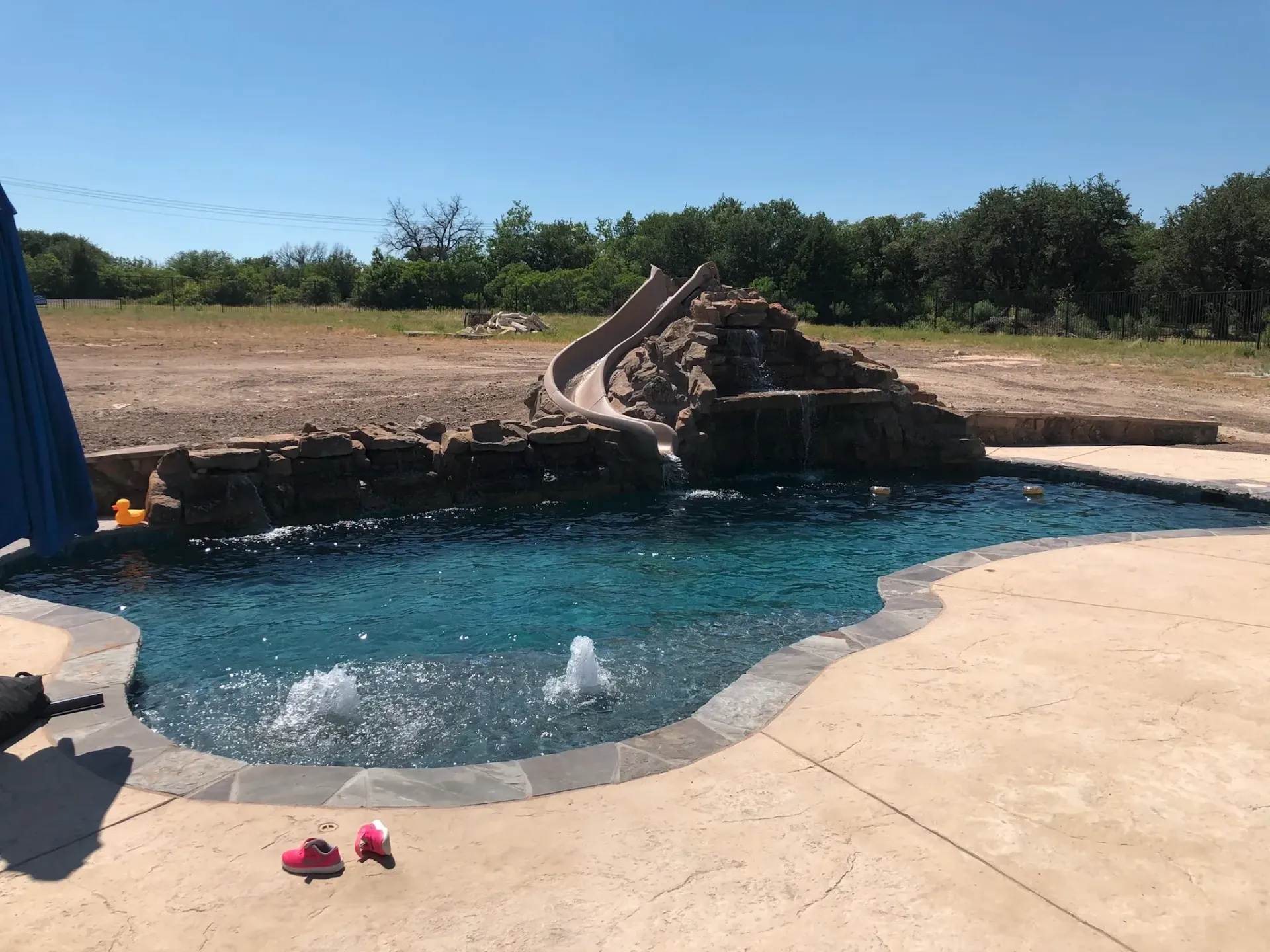 A large swimming pool with a water slide and a blue umbrella.