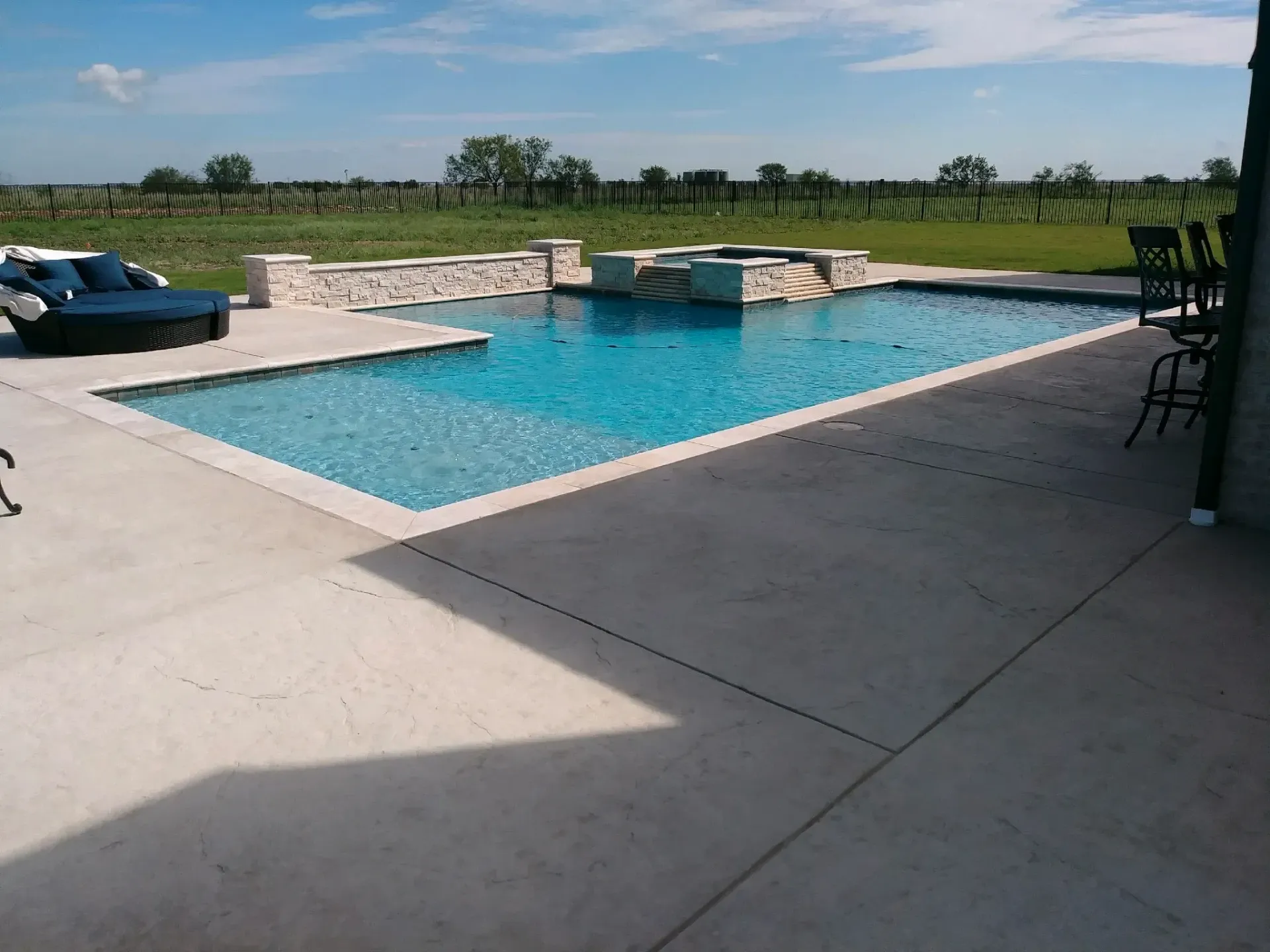 A large swimming pool is surrounded by a patio and chairs
