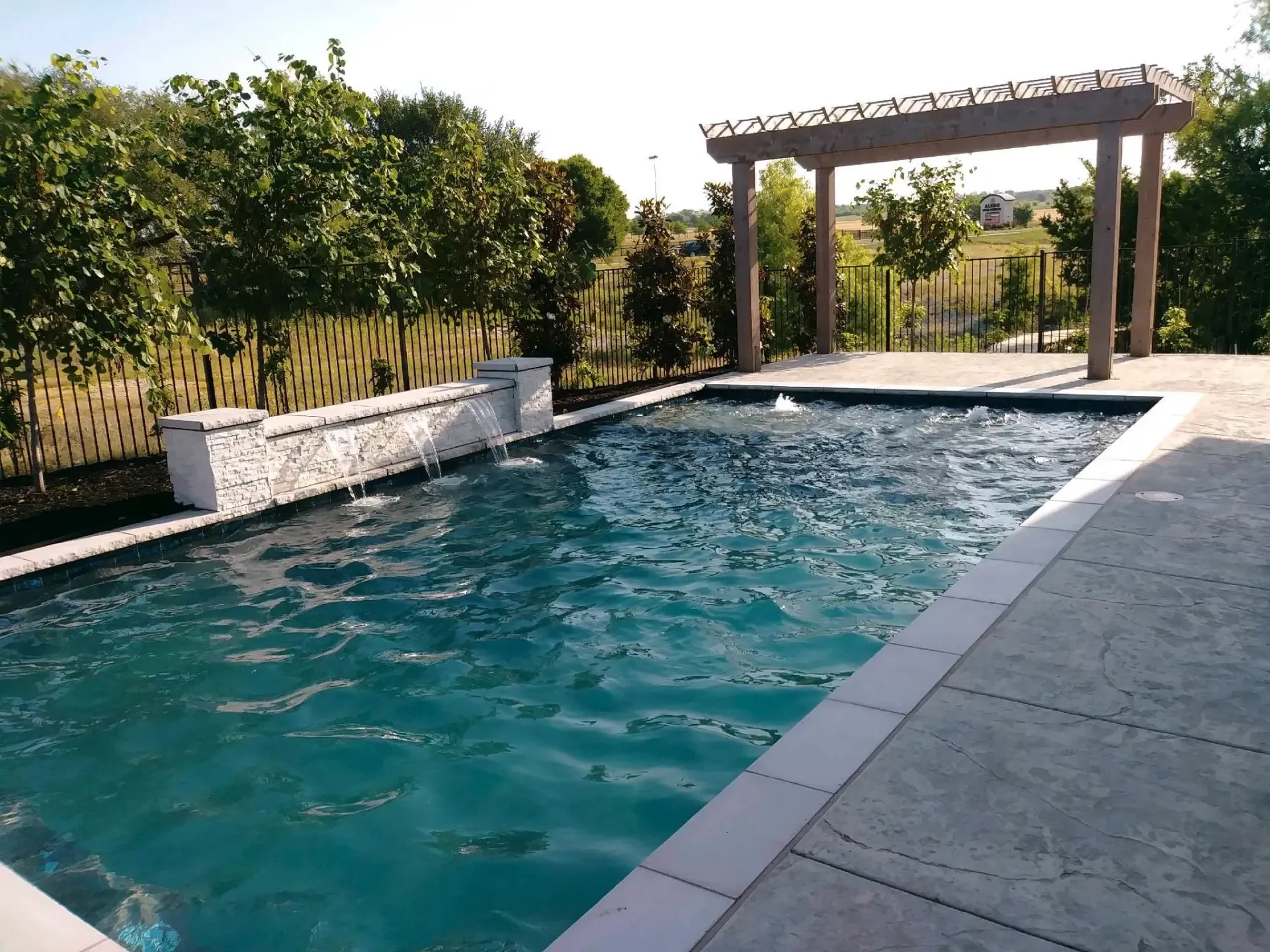 A large swimming pool with a pergola in the background
