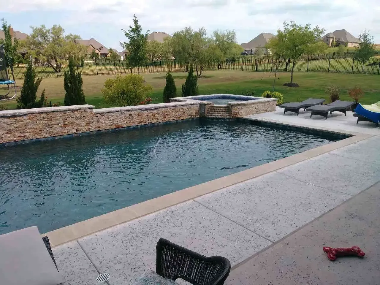 A large swimming pool is surrounded by lawn chairs and trees