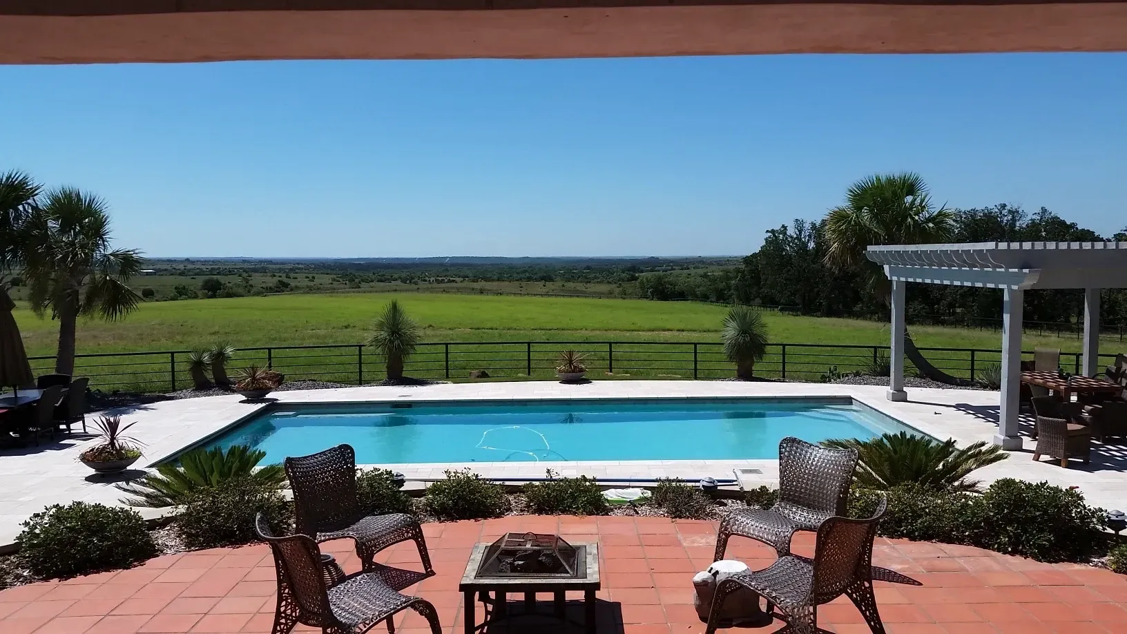 A large swimming pool is surrounded by chairs and a table
