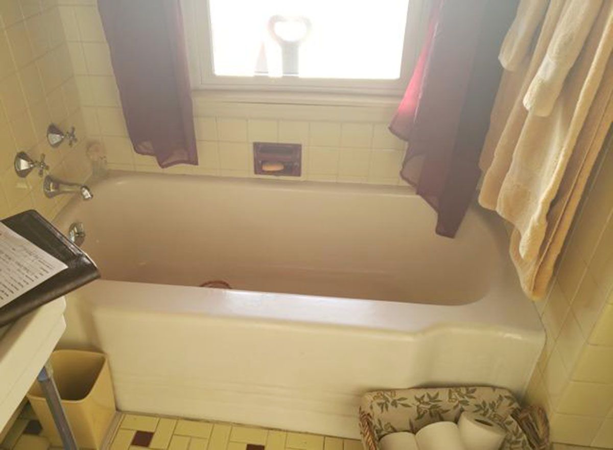 Bathroom with a white bathtub, tiled walls and floor, window, and towels hanging