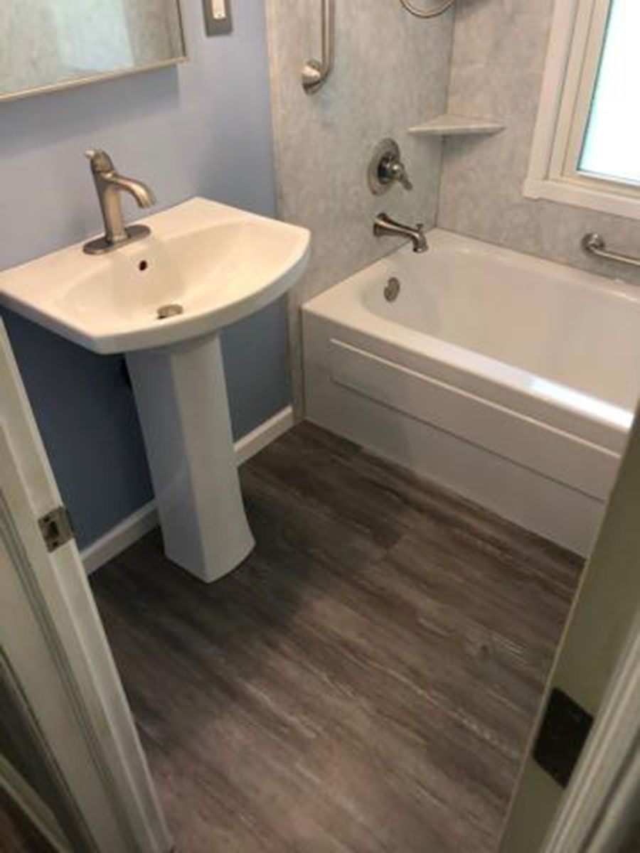 Bathroom with pedestal sink, tub, and gray wood-look flooring. Light blue walls