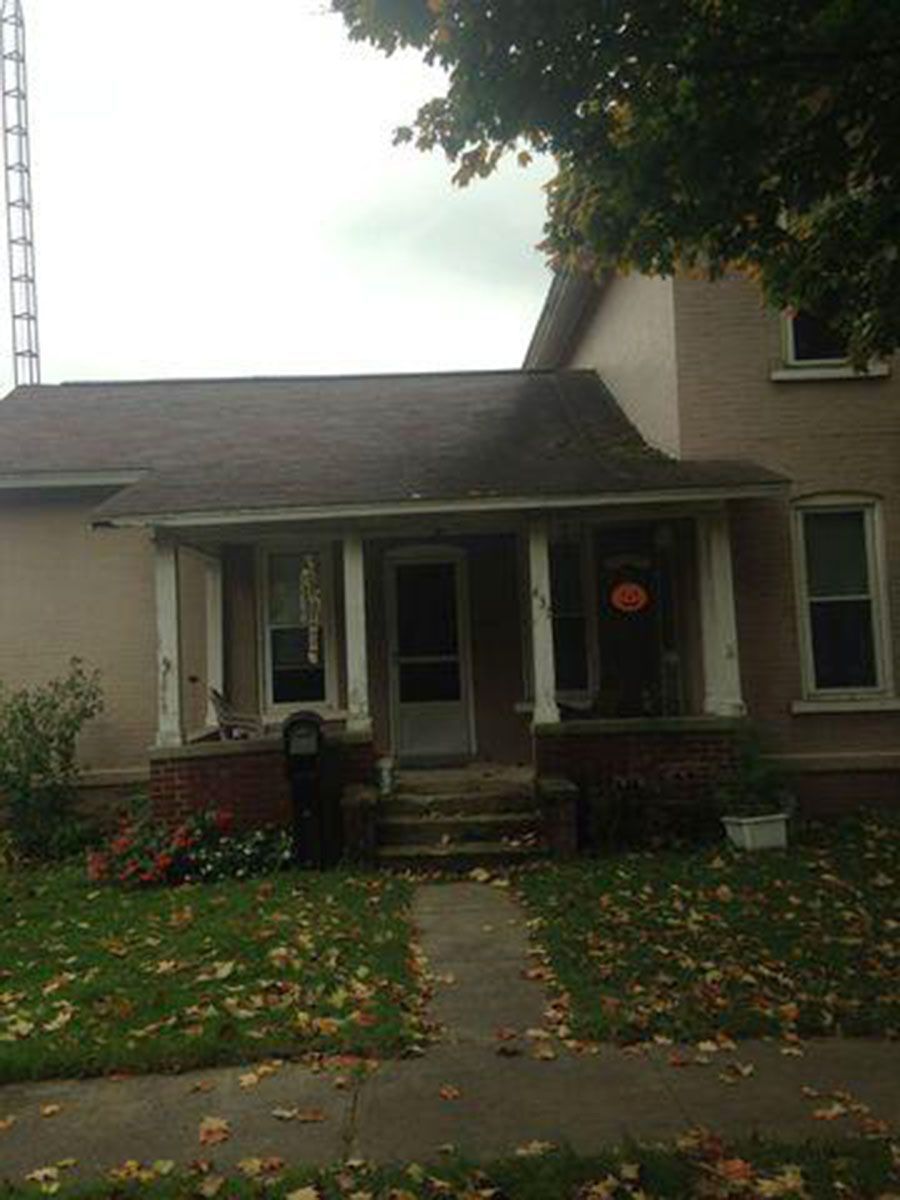 Tan house with porch and front door, a walkway leading to the entrance, a grassy lawn, and a tree
