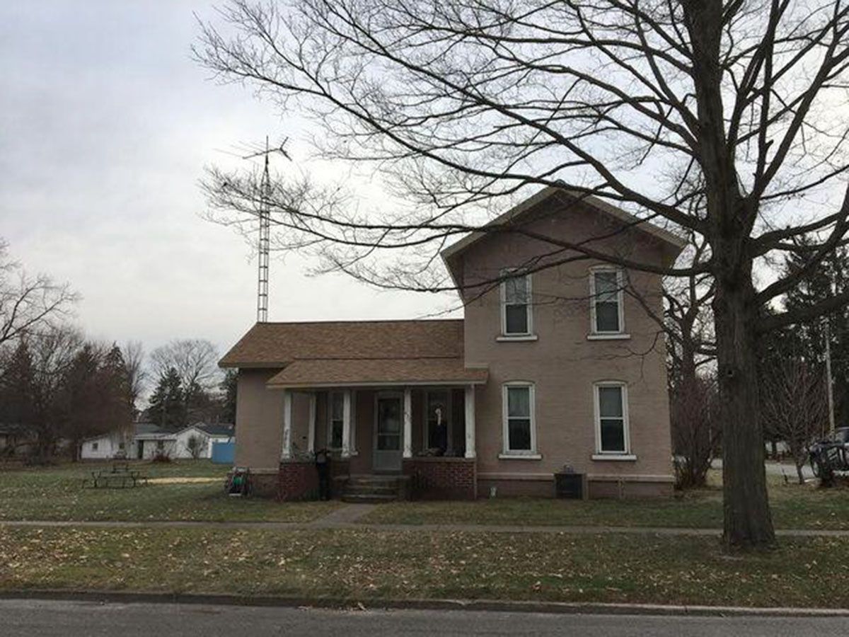 Two-story beige house with porch, bare tree in foreground, utility pole