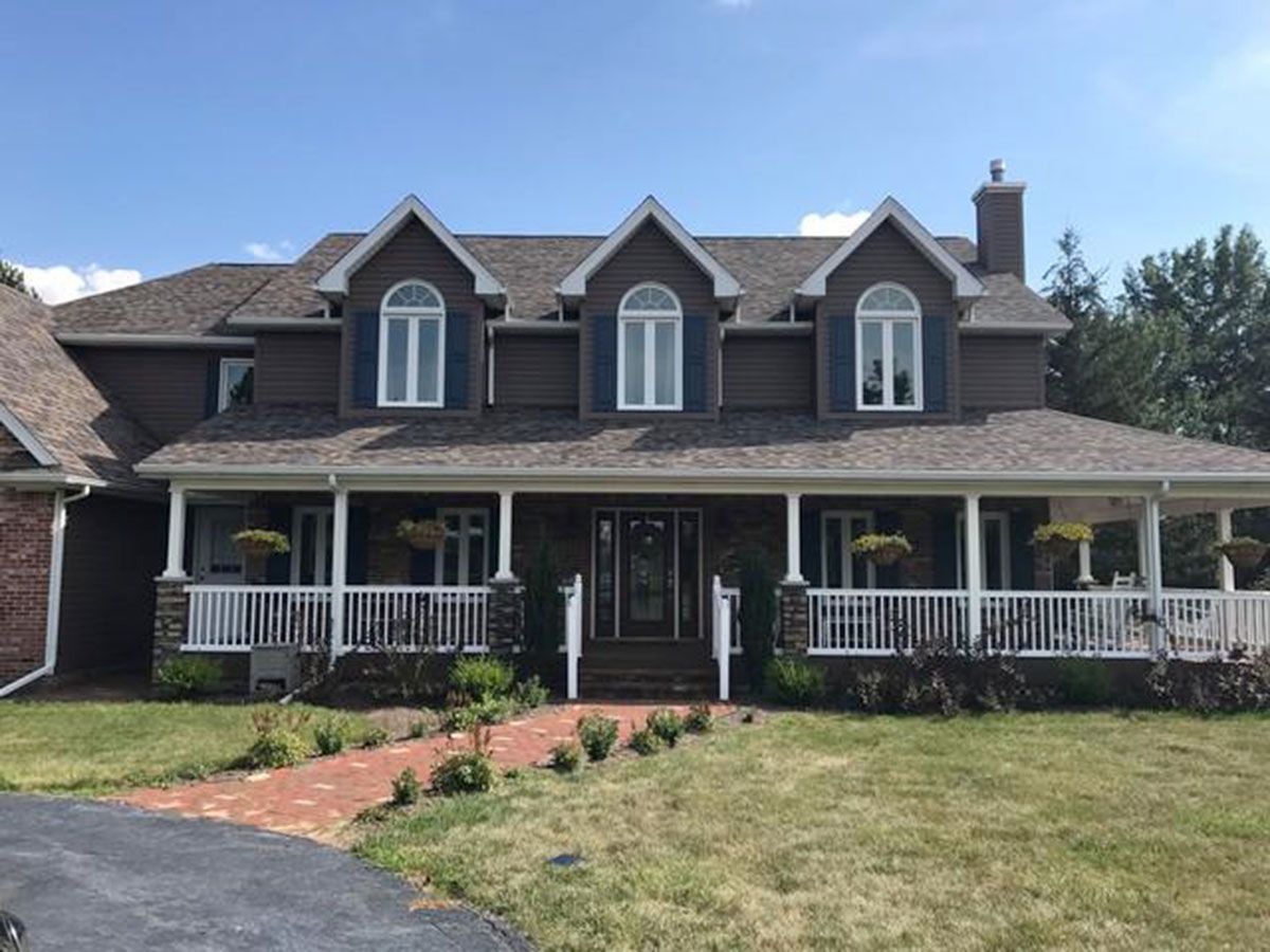 Brown house with white porch, brick walkway, and three arched windows