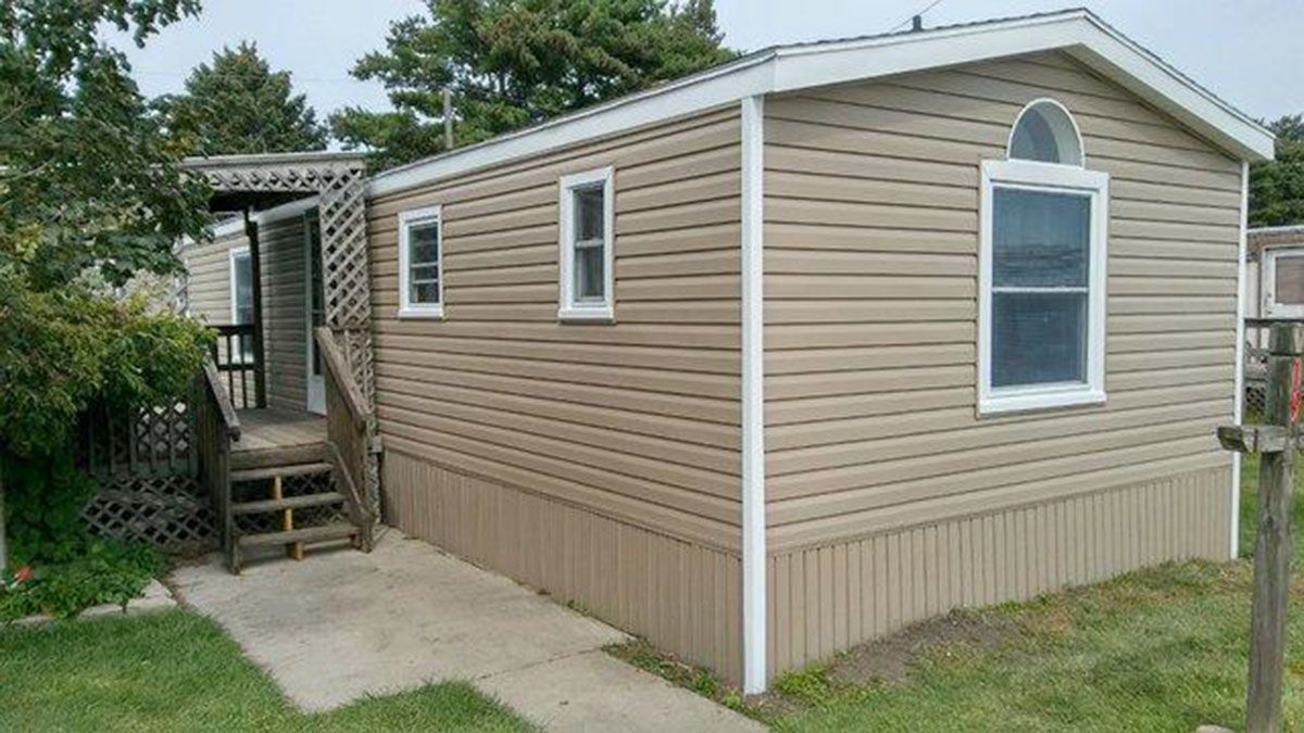 Mobile home with brown siding, white trim, and a concrete path leading to a wooden deck