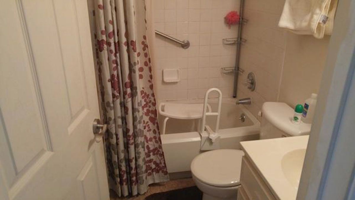 Bathroom with shower curtain, toilet, sink, and grab bars for accessibility