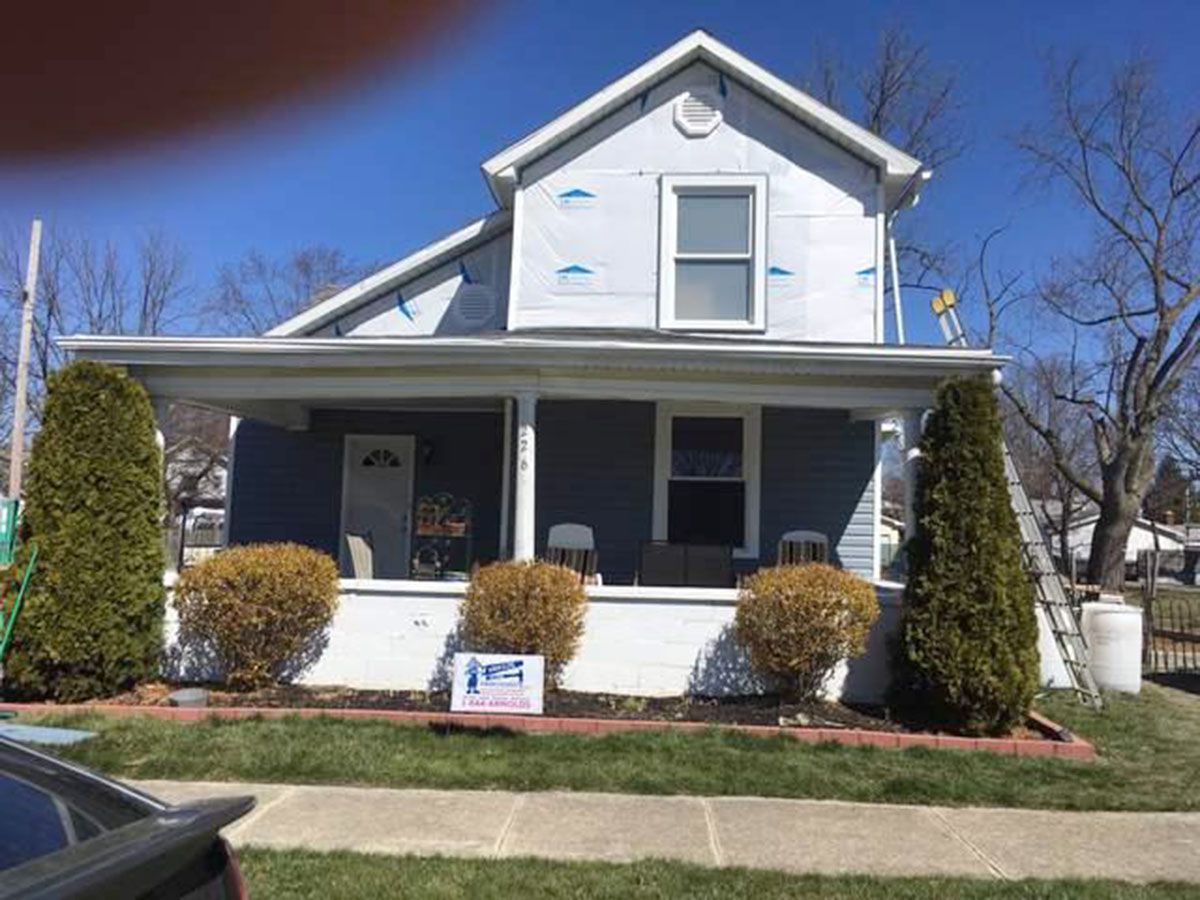 House exterior during renovation; blue siding, white trim, with insulation visible on the top half