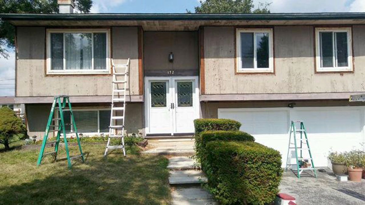 House exterior with white doors and windows; ladders are leaning against the house