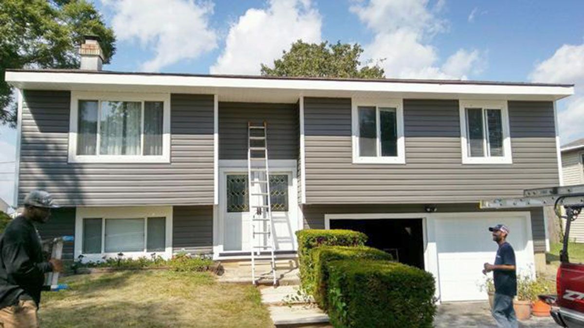 House exterior with gray siding, white trim, and a ladder; workers near it