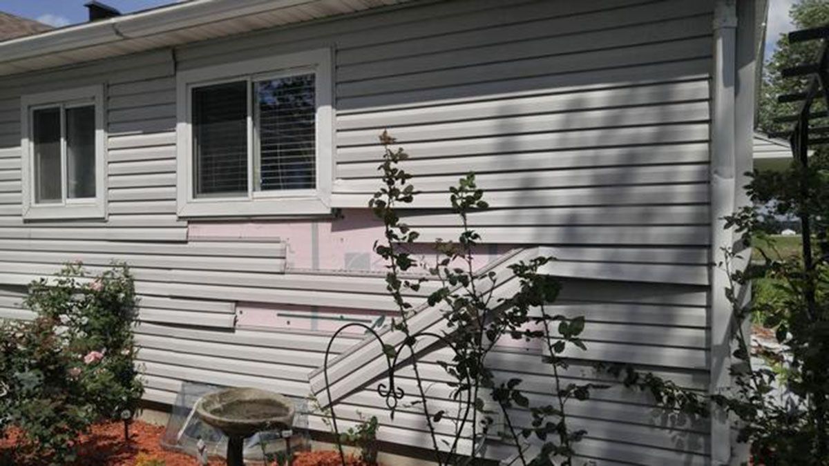 Exterior house siding damage near a window; exposed pink insulation