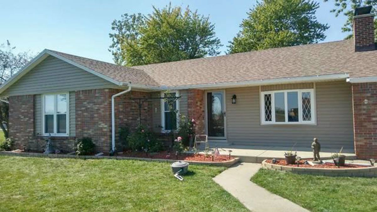 Tan and brick ranch home with green lawn and walkway on a sunny day