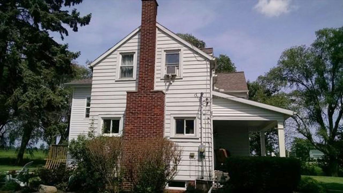 White two-story house with a brick chimney and a covered porch