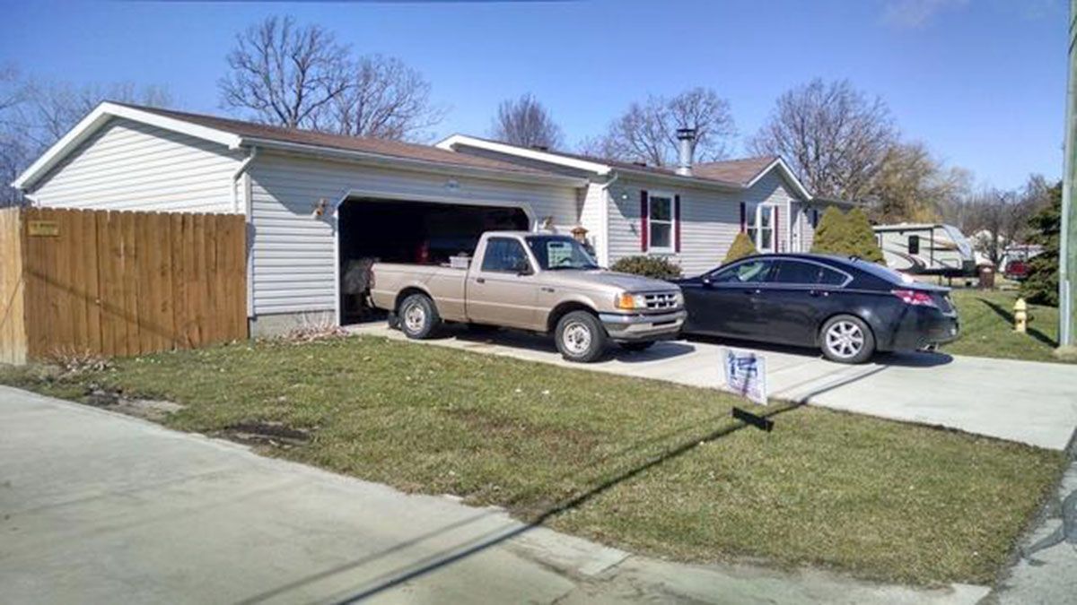 Tan pickup truck in garage, black sedan in driveway of a house on a sunny day