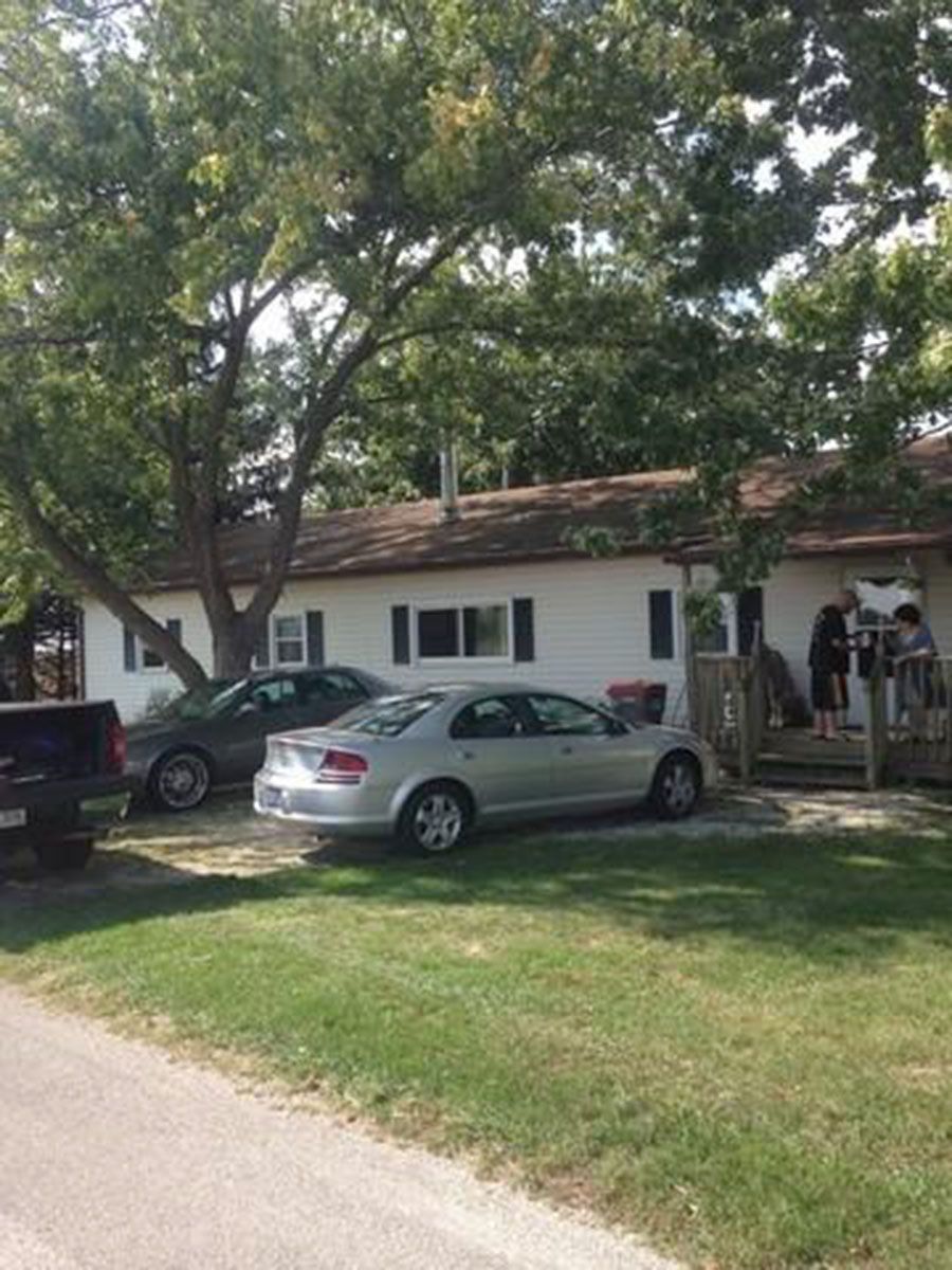 A white bungalow with cars parked in front and people on the porch