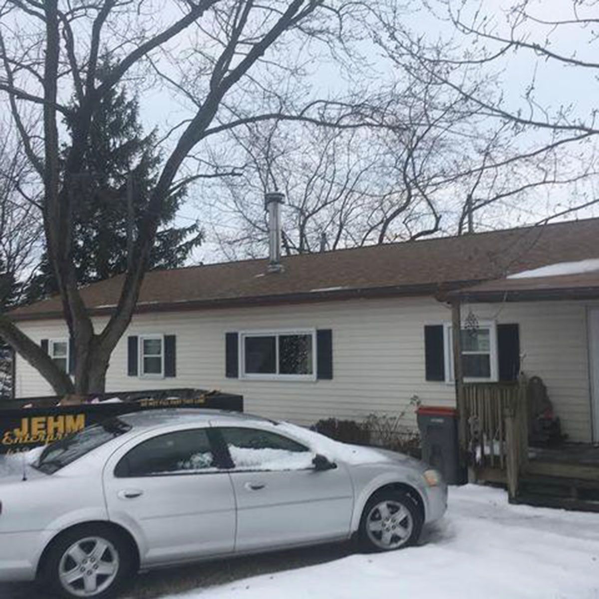 Silver car parked in front of a snow-covered house with a brown roof and a tall chimney