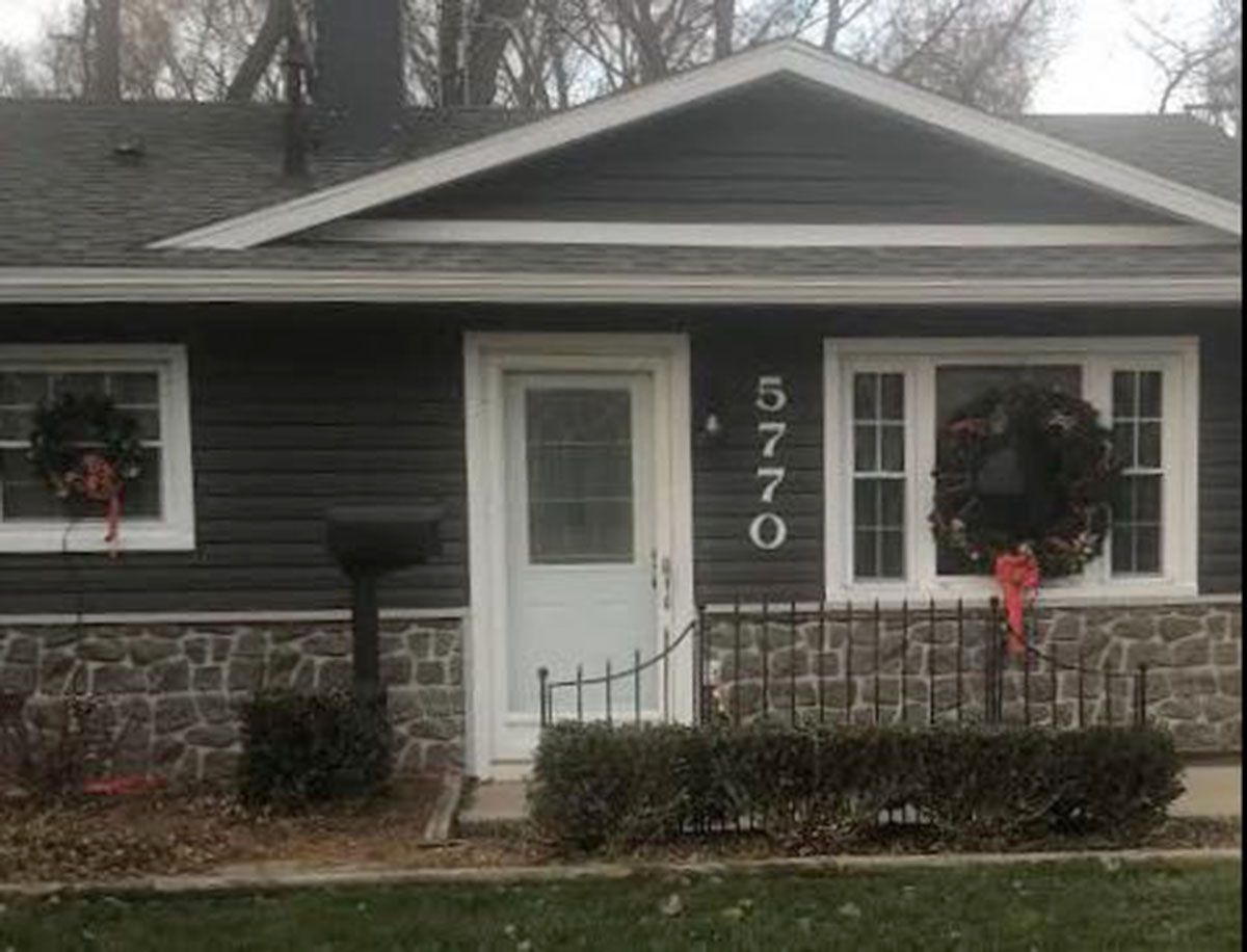 Dark gray house with white trim, stone base, and wreaths on windows