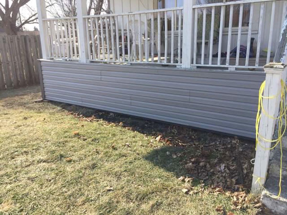 Gray siding covers the base of a porch with white railing