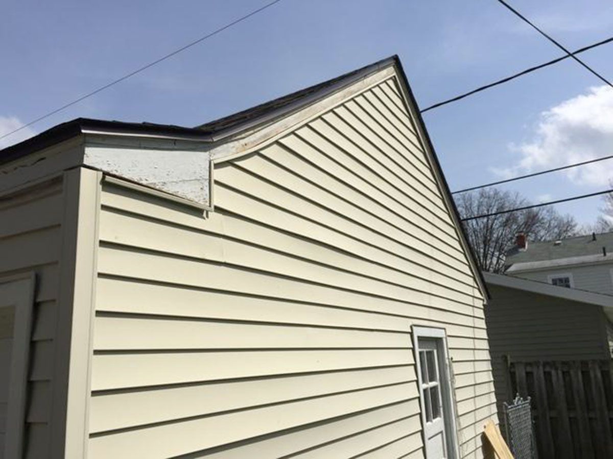 Beige siding on a gabled roof garage, with a small window and wooden trim