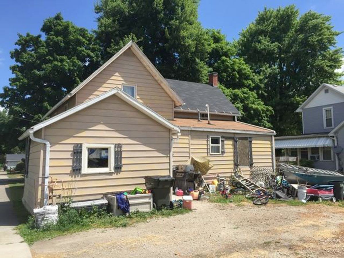 A two-story house with a cluttered backyard on a sunny day
