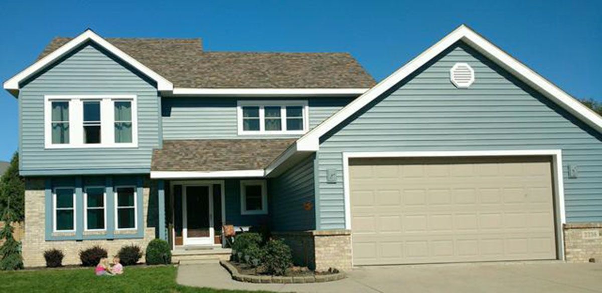 Blue-sided two-story house with tan garage door, brown roof, and blue sky