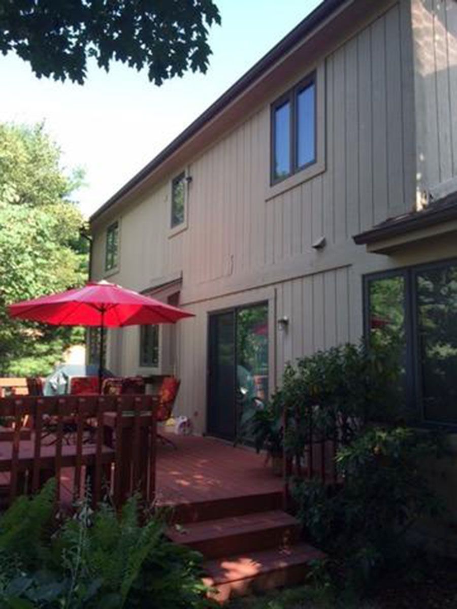 Red deck and umbrella beside a tan house with dark windows
