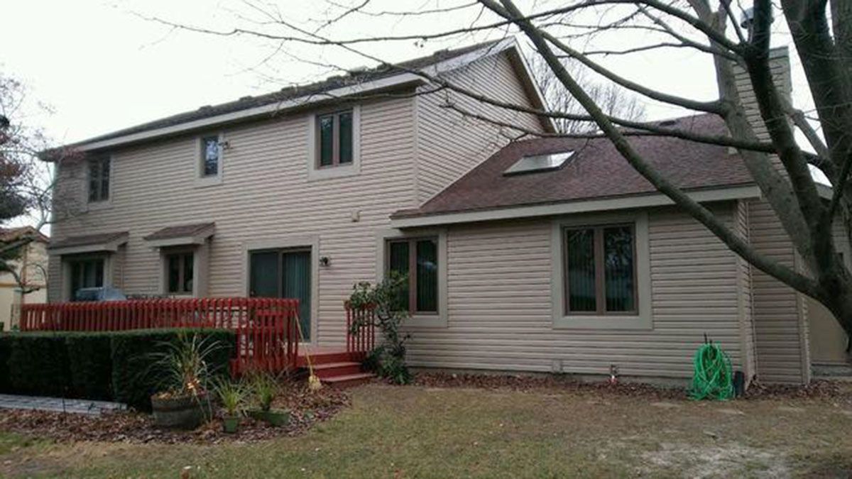 Back of a two-story beige house with a red deck and a green hose on the grass