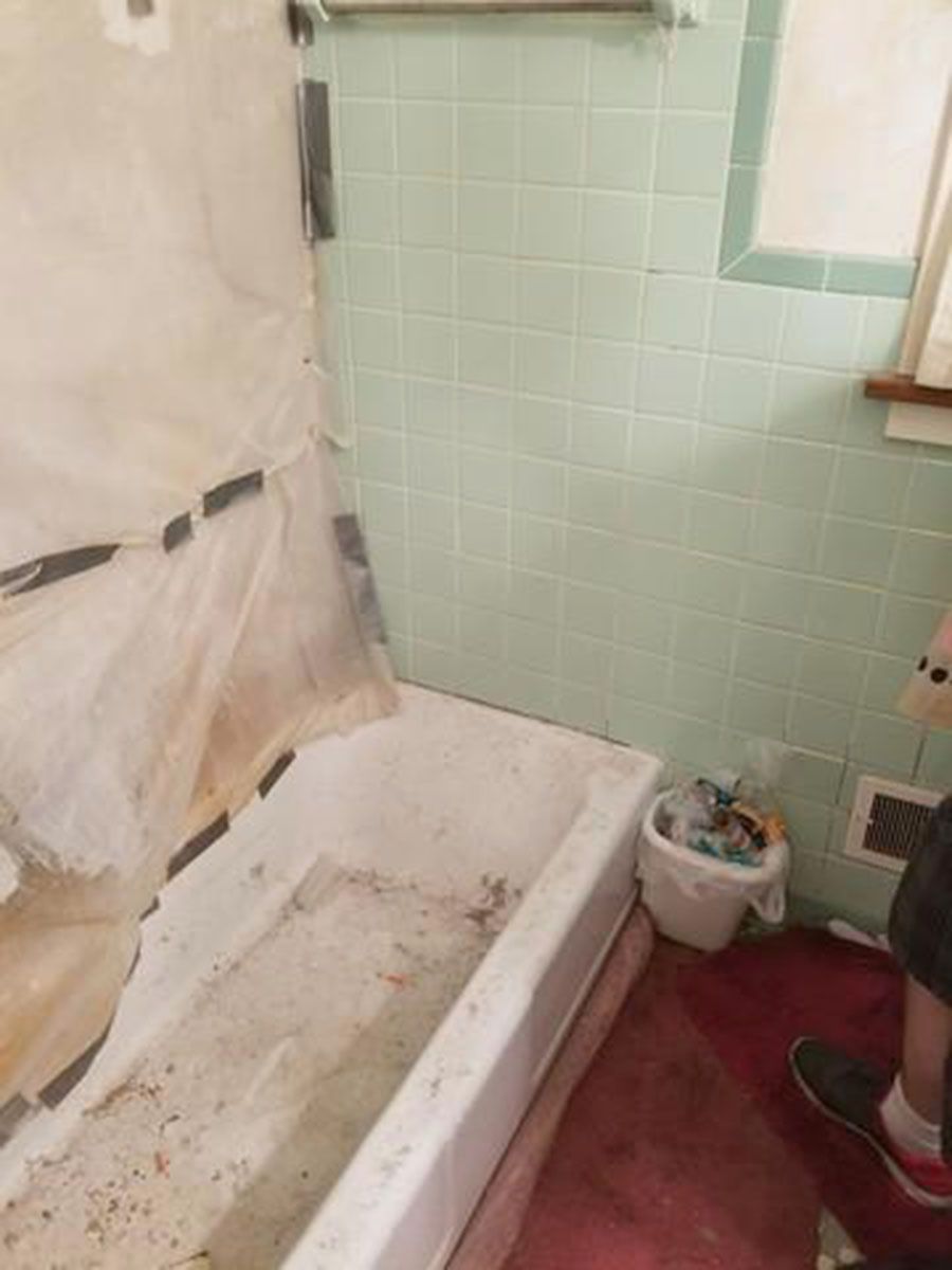 Dirty bathroom with a tub, green tiles, and a partially transparent shower curtain