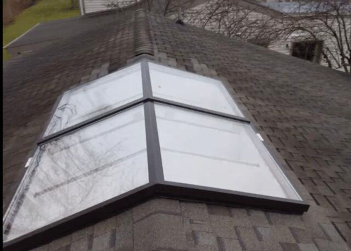 Skylight on a shingled roof, angled design, with dark metal frame and clear panes
