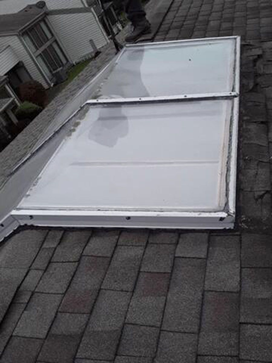 Skylight on a shingled roof, showing a rectangular glass pane in a white frame