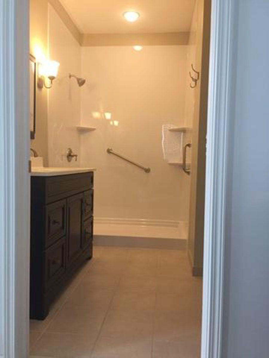 Bathroom with a dark vanity, accessible shower with grab bar, and neutral tile flooring